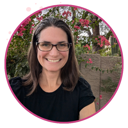 woman with glasses smiles in front of pink flowers